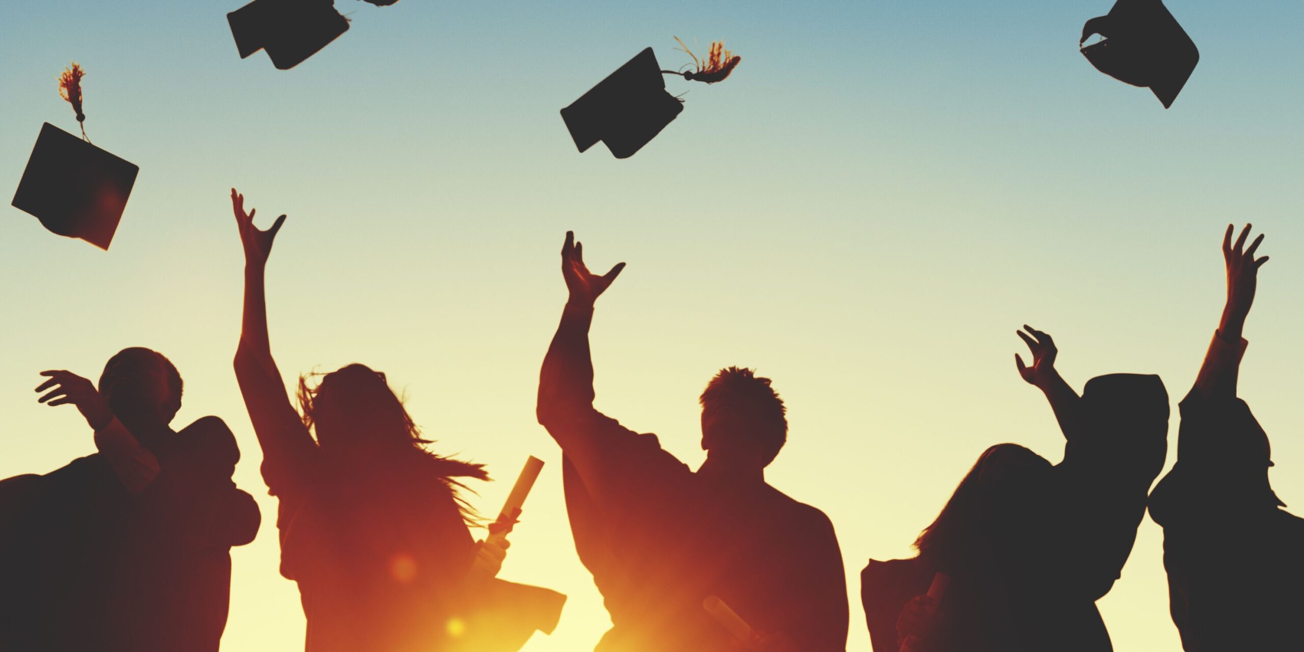 Graduates celebrating at sunset, tossing their caps in the air, symbolizing achievement and the end of their academic journey.