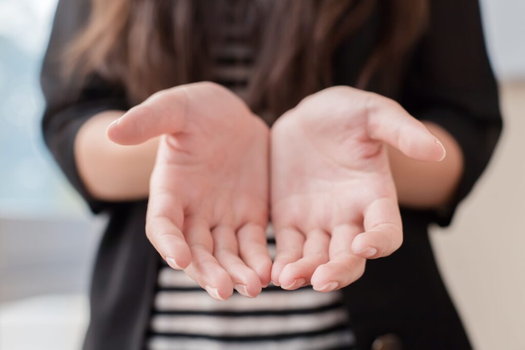 Open hands extended forward, symbolizing an invitation or offering. The background is soft-focused, emphasizing the hands as the main subject.