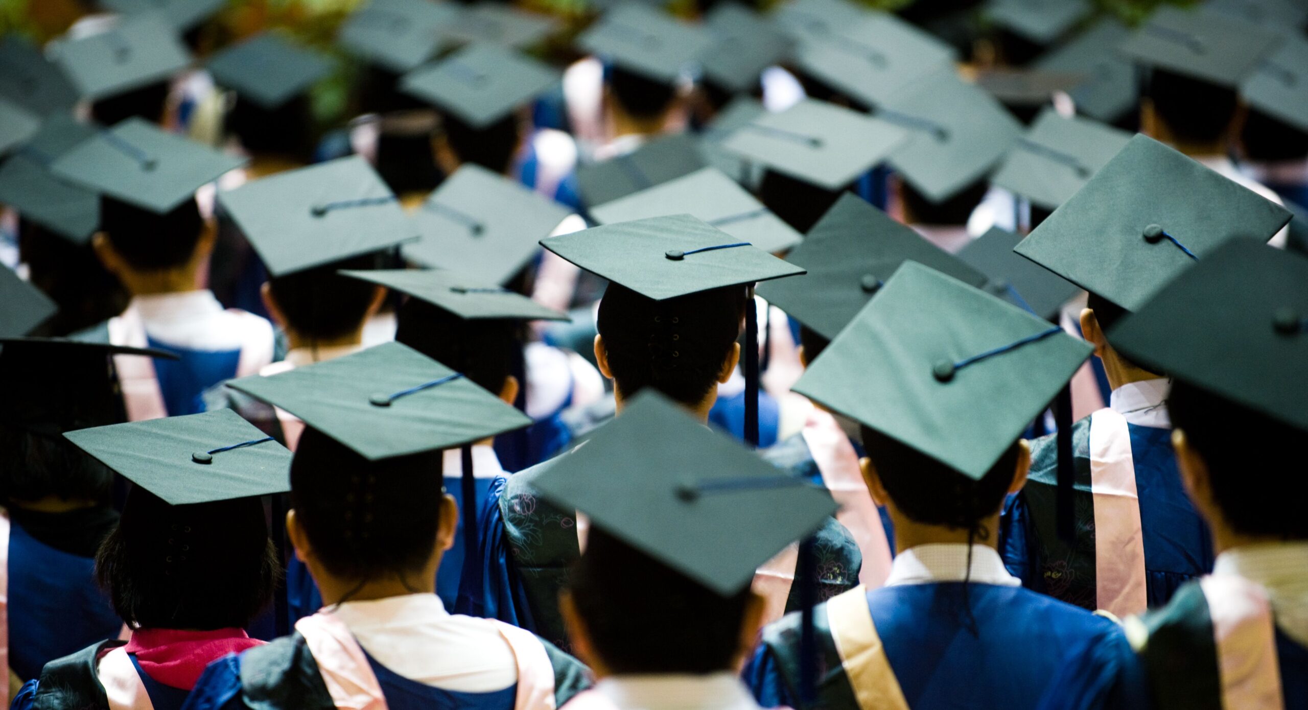 Graduates in caps and gowns stand together, celebrating their achievements during a graduation ceremony. The focus is on unity and accomplishment.