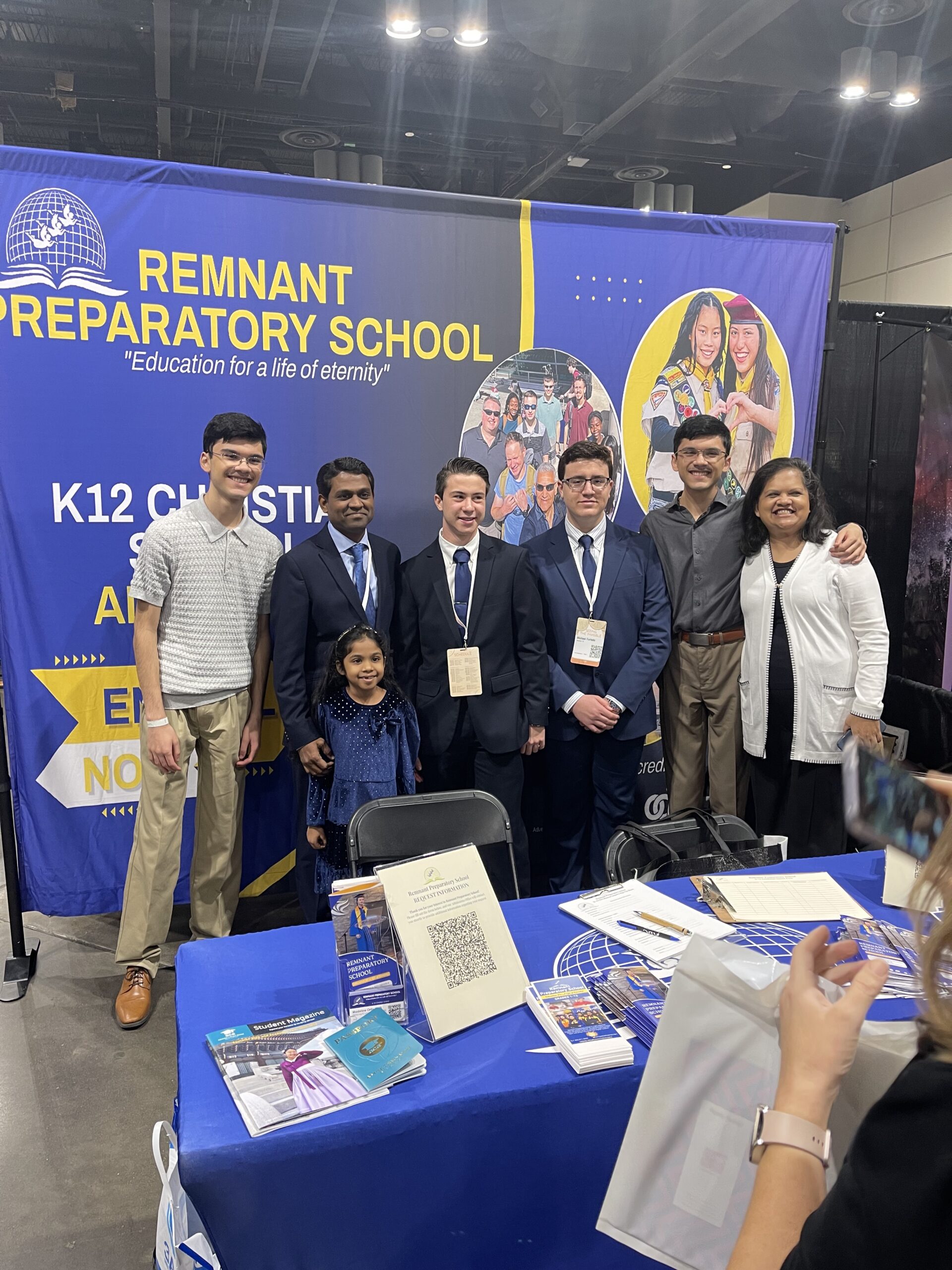 Group photo at the Remnant Preparatory School booth featuring staff and students, promoting K12 Christian education at an event.